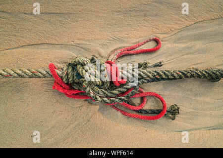 Creative red knotted ships rope lying on a sandy beach leading out to sea on the shoreline as the tide comes in. Stock Photo