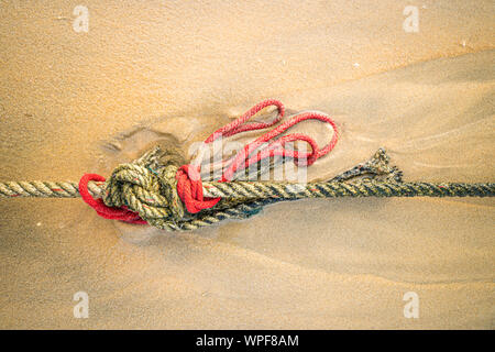 Creative red knotted ships rope lying on a sandy beach leading out to sea on the shoreline as the tide comes in. Stock Photo