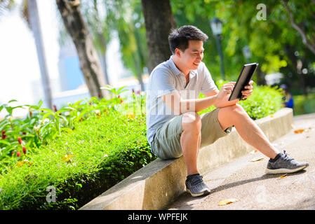 Young asian man using tablet in summer park Stock Photo