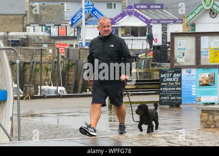 West Bay, Dorset, UK.  9th September 2019. UK Weather.  A dog walker strolling around the harbour on a day of heavy rain at the seasde resort of West Bay in Dorset.  Picture Credit: Graham Hunt/Alamy Live News Stock Photo