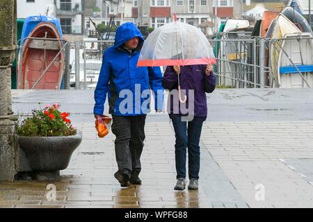 West Bay, Dorset, UK.  9th September 2019. UK Weather.  A couple with an umbrella walking near the harbour on a day of heavy rain at the seasde resort of West Bay in Dorset.  Picture Credit: Graham Hunt/Alamy Live News Stock Photo