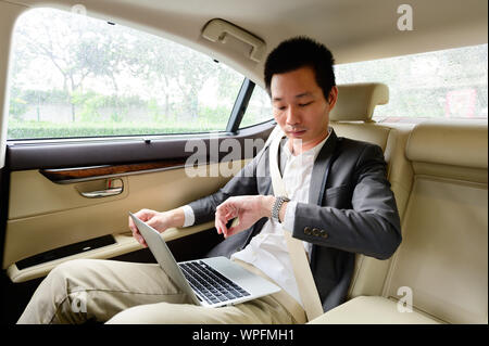 Handsome businessman checking time and working with laptop in car Stock Photo