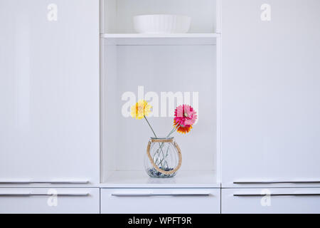 Minimalist white kitchen interior design with colorful flowers in vase. Glossy cupboard surface Stock Photo