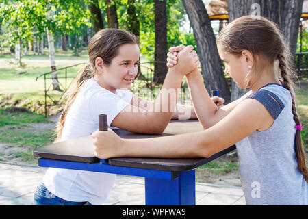 two teenage girls are engaged in arm wrestling closeup outdoor in city park Stock Photo