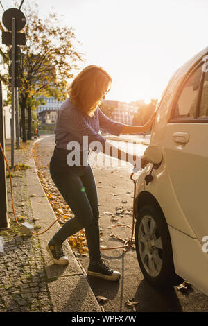 Young woman is charging carsharing electric car. Stock Photo