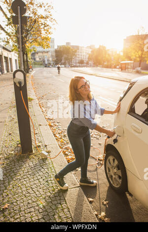 Young woman is charging carsharing electric car. Stock Photo