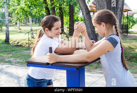 two teenage girls are engaged in arm wrestling closeup outdoor in city park Stock Photo