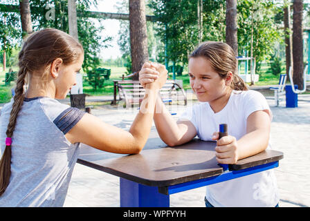 two teenage girls are engaged in arm wrestling closeup outdoor in city park Stock Photo
