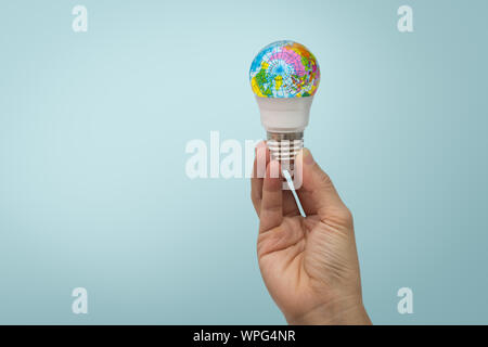 Hand is holding the LED bulb with the globe on blue background. Stock Photo
