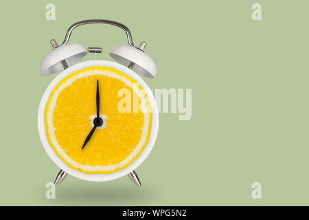 Creative fresh lime slice alarm clock on pastel green background, idea concept with copy space. Stock Photo