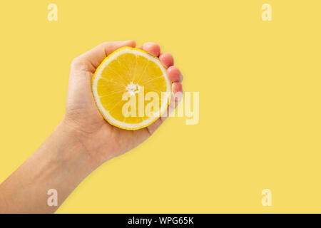 Female hand squeezing half of lemon on yellow background, Healthy eating and diet concept. Stock Photo