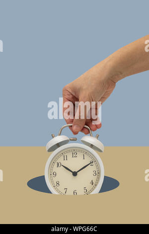 Hand holding white vintage alarm clock  on blue backdrop falling down. Time Minimal concept. Stock Photo