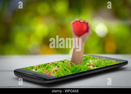 Hand holding a heart shaped ball emerges from the smartphone. Valentine or wedding concept. Stock Photo