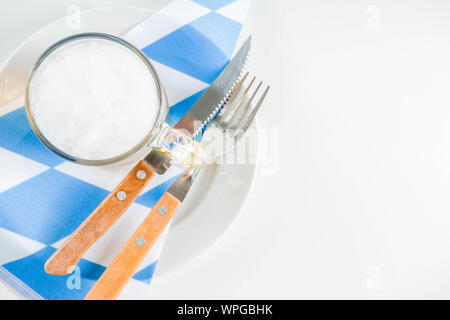 Oktoberfest festive cutlery set  with with a traditional checkered  tablecloth, plate, pretzel, fork, knife and a glass of beer. background for Restor Stock Photo