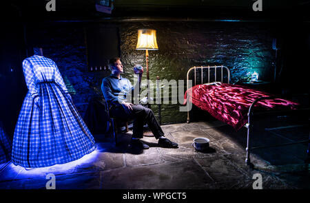 Museum employee Harry Jelley holds a model of an eyeball, as objects around him are lit by light from projectors to form part of the How My Light Is Spent installation by Frank Cottrell-Boyce at the Bronte Parsonage Museum in Haworth, West Yorkshire. Stock Photo