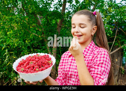 beautiful teen girl holding a bowl of raspberries in the garden closeup on summer day Stock Photo