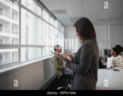 Side view of a creative female corporate worker using digital tablet in office with colleagues on background Stock Photo