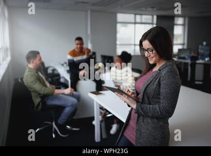 American Businesswoman using digital tablet by desk with colleagues discussing in background at office startup entrepreneur  Stock Photo
