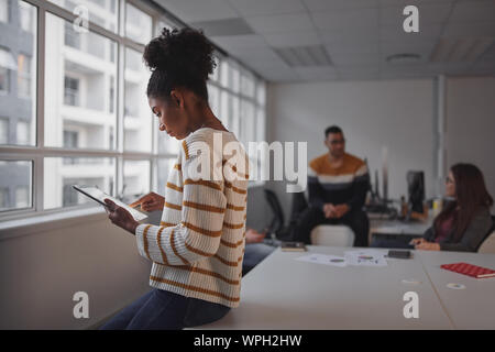 An african american young businesswoman working on digital tablet with Brazilian business team communicating in background Stock Photo