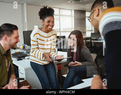 Creative young woman showing business plan on digital tablet to colleagues during a meeting in front of business group - start up company  Stock Photo