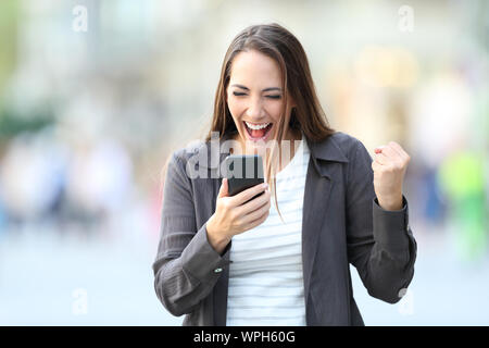 Front view portrait of excited woman checking smart phone on line content in the street Stock Photo
