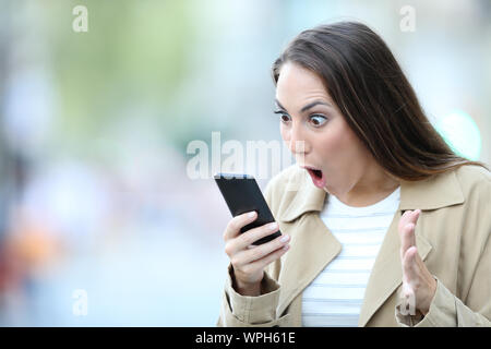 Shocked woman finding surprising news on smart phone in the street Stock Photo