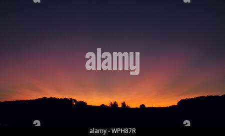 the sun setting behind a hill Stock Photo