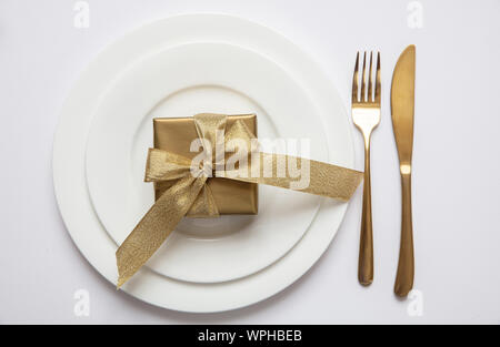 Festive dinner table setting, Gold gift box and cutlery on white set of dishes isolated, white background, top view Stock Photo