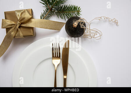 Xmas dinner table setting, Gold gift box and cutlery on white set of dishes, white background, top view Stock Photo