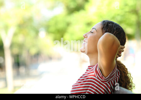 Side view portrait of a happy mixed race woman resting sitting on a bench in a park Stock Photo