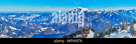 Alpine panorama from the top of Zwolferhorn mount with sharp peaks, rocky slopes, winter forests, blue Wolfgangsee and Mondsee lakes, St Gilden, Salzk Stock Photo