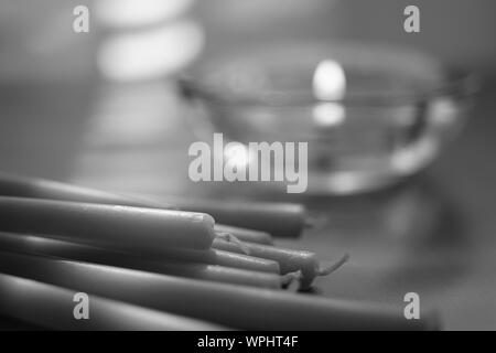 pile of new long candles and one low candle burns in a glass round candlestick, bw photo Stock Photo