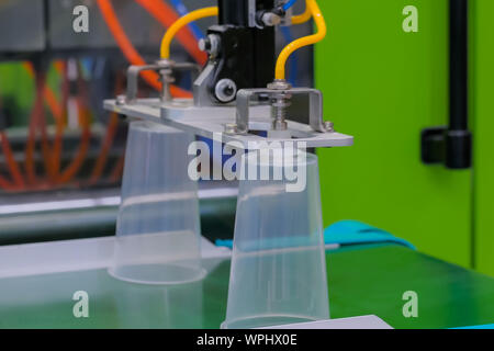 Cups on conveyor belt of plastic injection molding machine with robotic arm Stock Photo