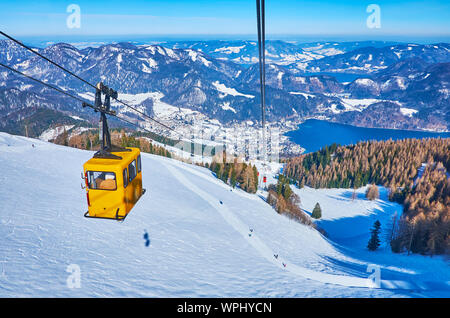 Spectacular view from the cable car on the Zwolferhorn mountain slope, skiers, going uphill, coniferous forest, Alps and deep blue Wolfgangsee lake in Stock Photo