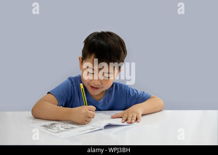 Asian boys are doing some writing on the book isolated on blue background. Stock Photo