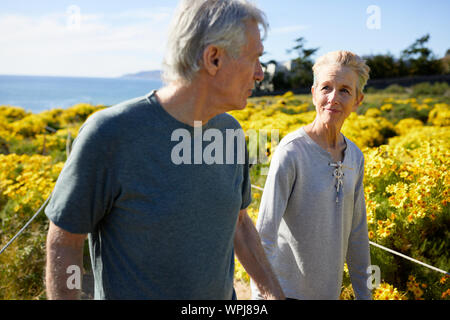 Senior couple looking at each other while walking on landscape during sunny day Stock Photo