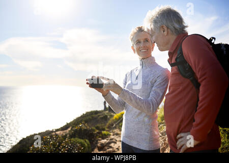 Smiling senior woman looking at man while holding smart phone against sky Stock Photo