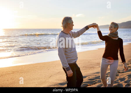 Smiling senior couple dancing at beach during sunset Stock Photo