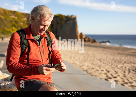 Senior man using smart phone while standing at beach Stock Photo