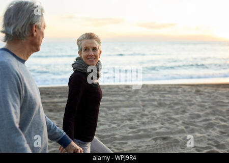 Side view of senior couple holding hands while walking at beach during sunset Stock Photo