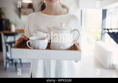 Autumn sseries in the Kitchen, melancholy and warm.. Relaxing in cold weather. red-haired girl holding a tray with cups and kettle Stock Photo