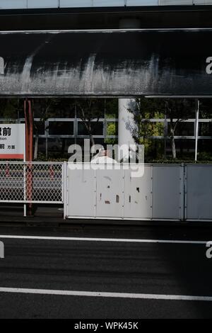 MATSUYAMA, JAPAN - Jul 30, 2019: A vertical shot of a person wearing a black cap sitting at a bus stop Stock Photo