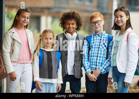 Group of multiethnic elementary students in casual clothing standing together and smiling at camera outdoors Stock Photo
