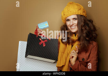 Hello autumn. 40 year old woman in yellow beret and scarf with credit card and shopping bags on brown background. Stock Photo