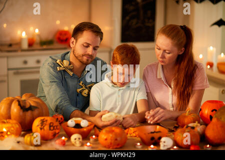 Mother and father sitting at the table together with their son and helping him to make a lantern from pumpkins for Halloween Stock Photo