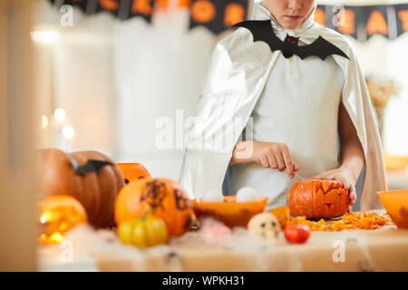 Close-up of bou dressed in costume standing near the table and making lantern from pumpkin for Halloween holiday Stock Photo