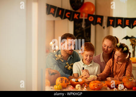 Happy family of four sitting at the table together decorating pumpkins and preparing for the Halloween holiday Stock Photo