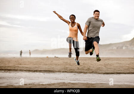 Smiling young couple jumping over shallow water on a beach. Stock Photo
