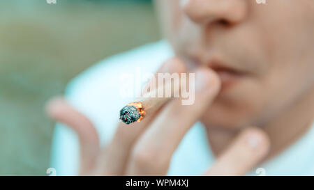 The young person smoking medical marijuana joint outdoors. The young man smoke cannabis blunt, close-up. Cannabis is a concept of herbal medicine. Stock Photo