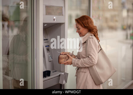 One mature woman, using ATM machine, putting her credit card in a wallet. Stock Photo